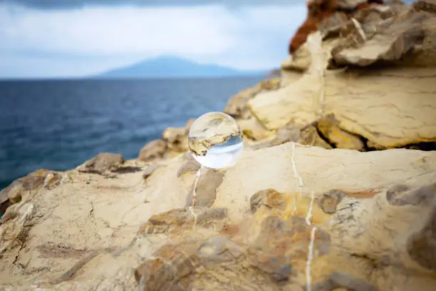 The sea is reflected in a glass ball against the background of a yellow stone. Texture of a rock close up.