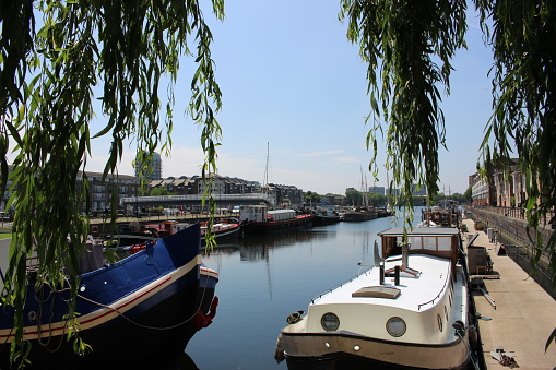 Canal Boats In Greenland Quay Dock, Surrey Quays, Canada Water, London Docklands next to the river thames on a sunny day. London skyline, housing boats and water.