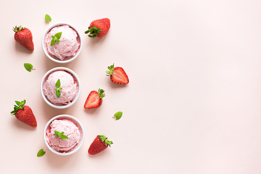 Strawberry ice cream and fresh strawberries on pink background, top view. Three bowls of strawberry ice cream, healthy summer dessert.