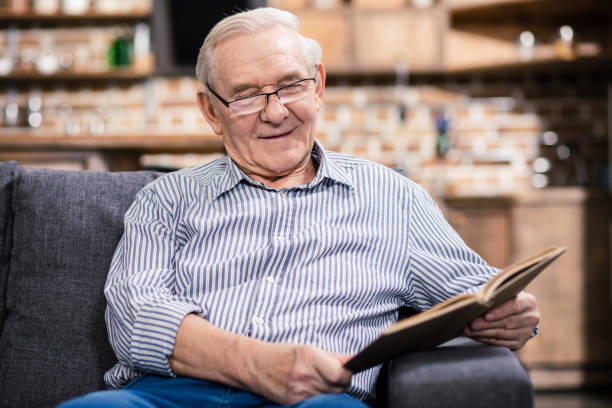 istock Cheerful aged man in glasses reading a book 983347394