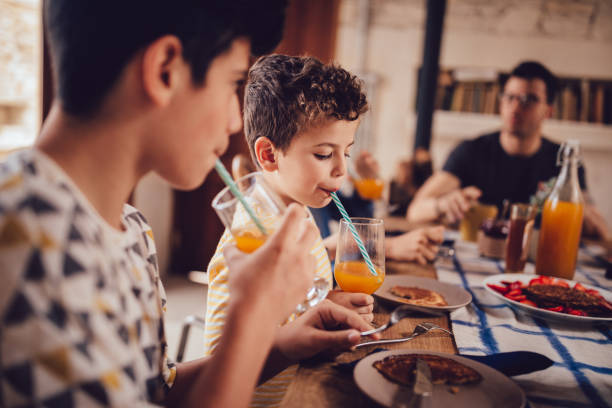 boys trinken frischen gepresster orangensaft beim frühstück mit der familie - breakfast eating people teens stock-fotos und bilder