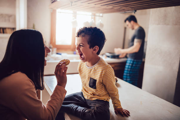 madre alegre dando galletas de hijo pequeño en la mañana - healthy eating snack child domestic kitchen fotografías e imágenes de stock