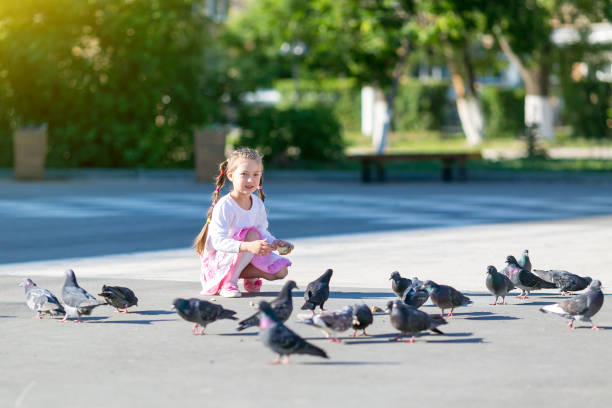 Beautiful girl gives bread to the birds on the city street.