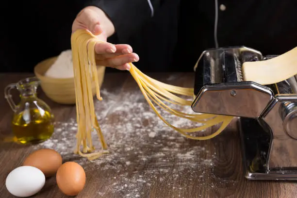 Photo of Chef making spaghetti noodles with pasta machine.