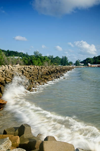 istock costline scenery with blue sky, clouds and waves hitting breakwater. 983406724