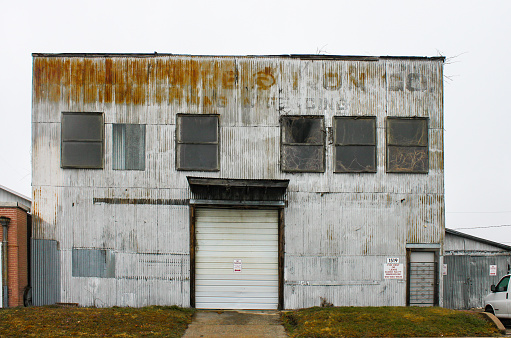 Old sheet metal industrial building with faded lettering and plants growing in windows and out of roof and for rent sign Tulsa OK USA 2 23 2016