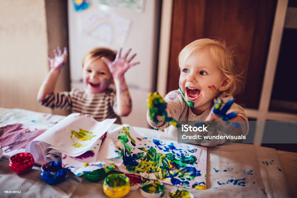 Cheerful little children having fun doing finger painting Happy little girls with dirty hands and faces having fun being creative with finger painting Child Stock Photo