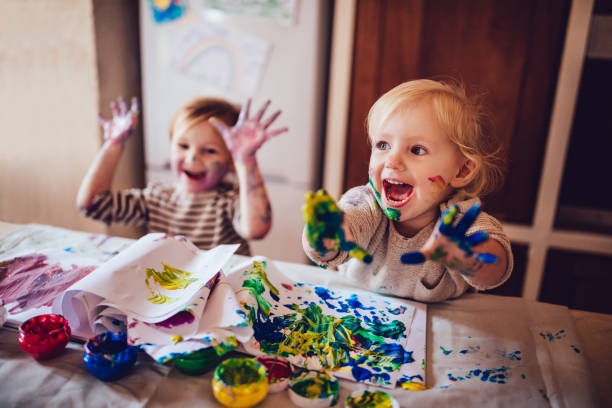Cheerful little children having fun doing finger painting Happy little girls with dirty hands and faces having fun being creative with finger painting messy stock pictures, royalty-free photos & images