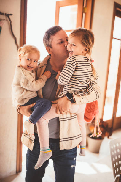 istock Affectionate father holding and kissing little daughters at home 983421288