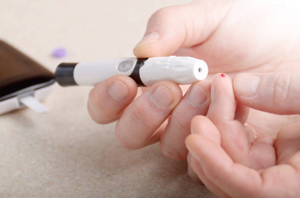istock Man Pierce his fingertip before doing blood test with personal glucometer 983494148