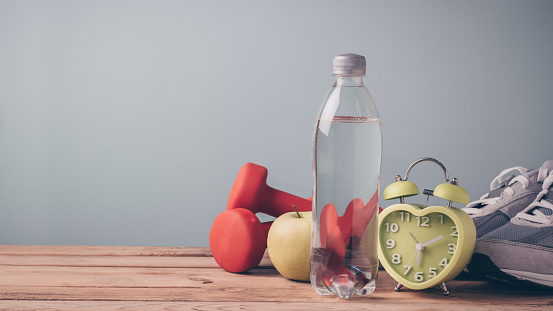 Fitness background with bottle of water, apple, dumbbells and sport shoes on wooden table