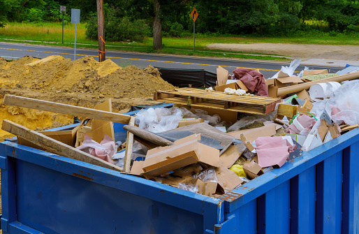 Blue construction debris container filled with rock and concrete rubble. Industrial garbage bin