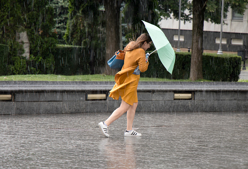 Belgrade: One young woman running under umbrella in the sudden  heavy spring windy rain in the city park , holding a bottle of water