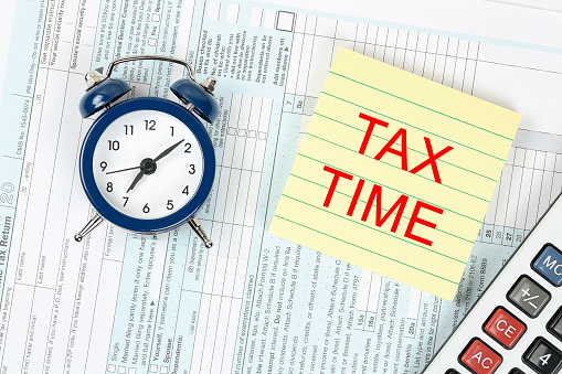 alarm clock, yellow note and calculator on 1040 tax form