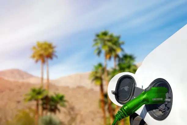 Close up view of Electric Car charging in the desert with palm trees and hills in the background.
