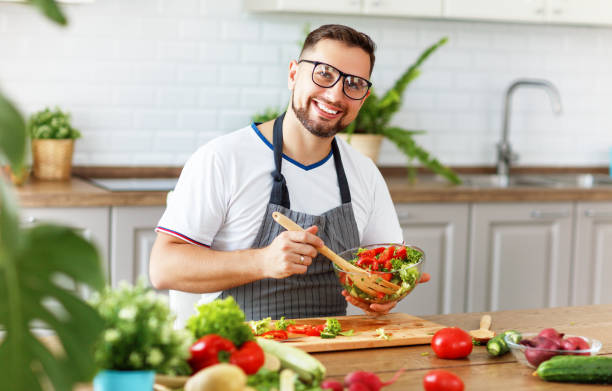 istock happy  man preparing vegetable salad in kitchen 983671622