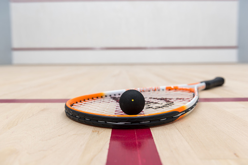 Close up of a squash racket and one-dot ball lying on the floor of a racquet court
