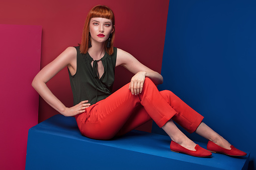 Fashionable redhead lady with fringe and glamour makeup posing over colorful background, looking at camera.