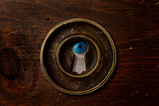 Extreme close-up of men’s blue eye looking through the keyhole.