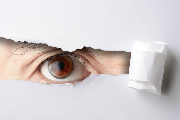 istock Brawn eyes looking through from a ripped hole in white paper 983783456