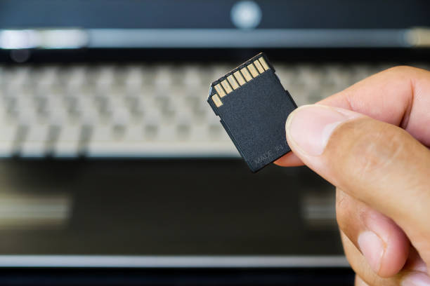 istock Hand holds SD Card against laptop pc. 983800550