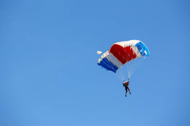 istock isolated skydiver  control colorful parachute gliding after free fall jump with blue sky background 983927912