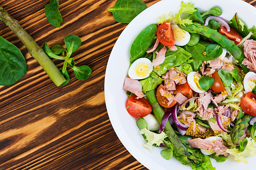 Salad with tuna, tomatoes, quail eggs, asparagus and onions on wooden background
