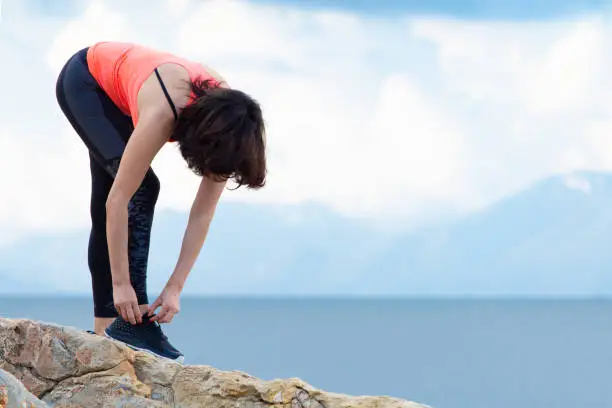 A woman ties up her shoelaces on sports shoes for fitness on the seashore.