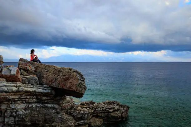 A woman rests on the rocks by the sea. She is wearing sports clothes for fitness.
