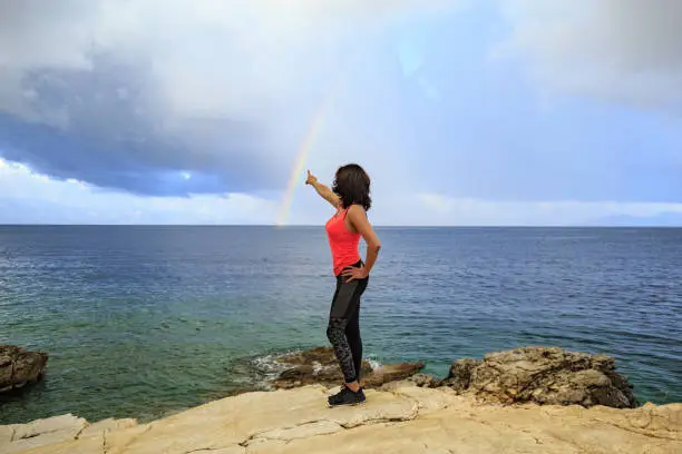 A middle-aged woman enjoys loneliness after exercising. She draws a rainbow over the sea after fitness.