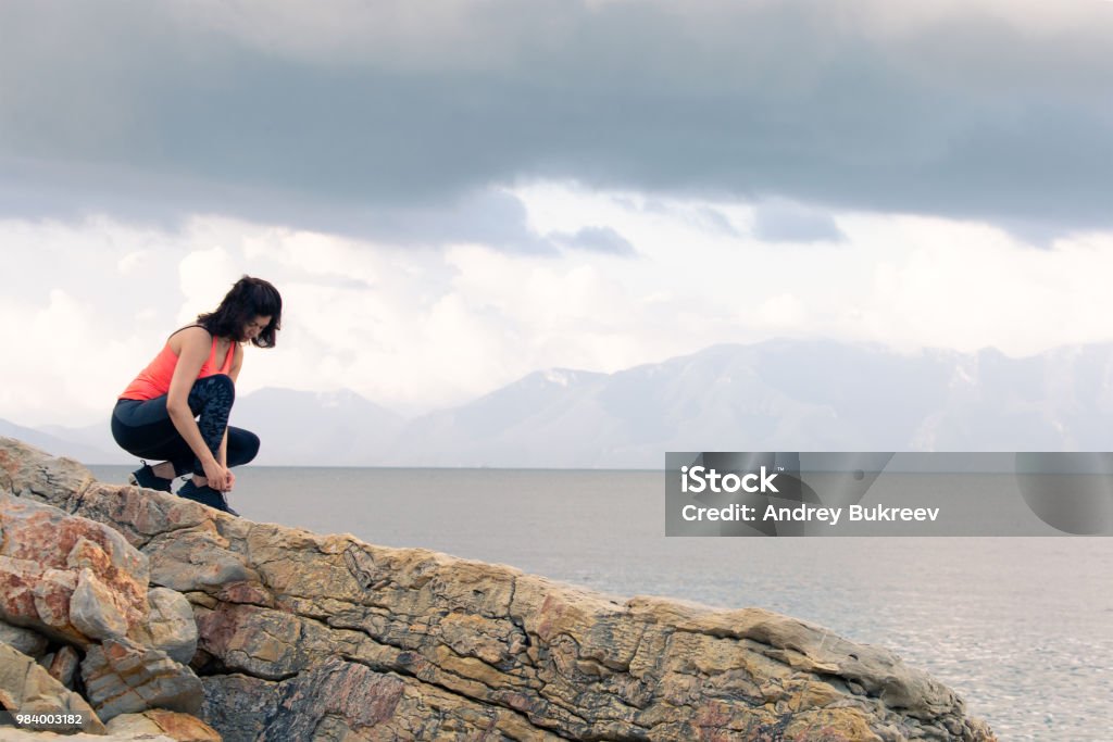 A middle-aged woman A woman ties up her shoelaces on sports shoes for fitness on the seashore. Active Lifestyle Stock Photo