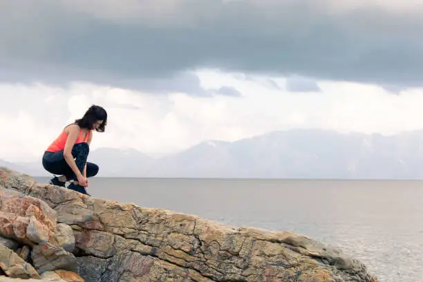 A woman ties up her shoelaces on sports shoes for fitness on the seashore.