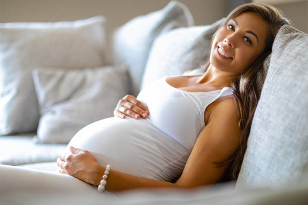 istock Smiling pregnant woman lying on the sofa touching her belly 984003836