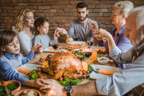 istock Extended family holding hands and praying before Thanksgiving dinner at dining table. 984007146