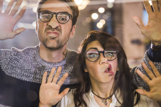 Playful colleagues having fun while sticking their faces on glass wall.