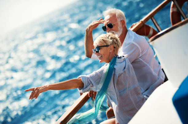 Senior couple on a sailing cruise. Closeup side view of mid 60's couple enjoying a sailing cruise during  summer vacation at seaside. They are leaning on deck railing and enjoying the view of the sea and horizon. old boat stock pictures, royalty-free photos & images