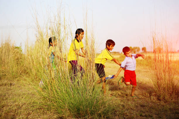 Two girls and a boy are laughing while seated on a colorful spring seesaw in the park with trees in the background. Two and four years old girls and a 3 year old boy share laughter while seated on a colorful spring seesaw in the park, with vibrant trees in the background, enjoying playful moments together