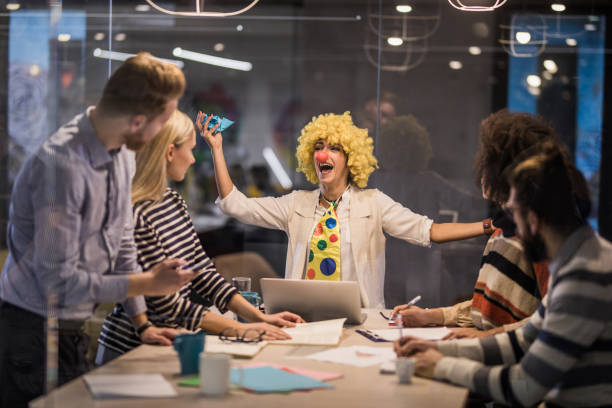 Playful businesswoman making a clown of herself on a meeting in the office. Young businesswoman having fun while pretending to be a clown on a meeting in the office. The view is through glass. fool stock pictures, royalty-free photos & images