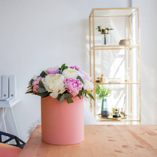istock Flower delivery to office. Working space, table with notebooks and magazines. Luxurious bouquet of peonies in pink box. 984023036