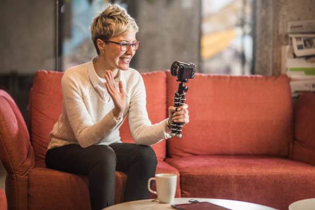 Happy woman waving while vlogging at casual office.