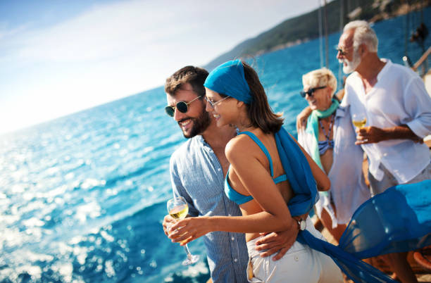Sailing cruise leisure. Closeup side view of mid 20's couple looking at sea and enjoying their sailing trip while sipping some sparkling white wine. There's mature couple in the background. passenger craft photos stock pictures, royalty-free photos & images