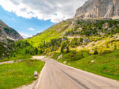 Asphalt road, green meadows and dolomite rocks at Passo Falzarego, Dolomites, Italy