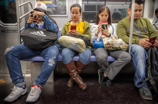 Four people checking their mobile phones in the subway Manhattan, New York, USA – May 11, 2018:  Four people checking their mobile phones in the subway train interior stock pictures, royalty-free photos & images
