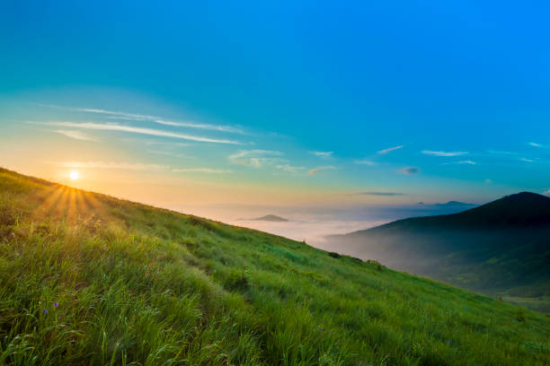istock Sunrise over hills in mountains with green grass and blue sky with white clouds 984093232