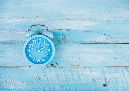 Blue alarm clock on blue wooden background and top view.