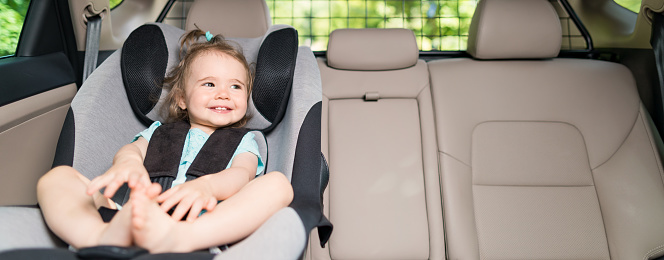 Beautyful smiling baby girl fastened with security belt in safety car seat