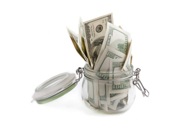 istock A glass jar filled with dollars among a hundred dollar bills. 984134174