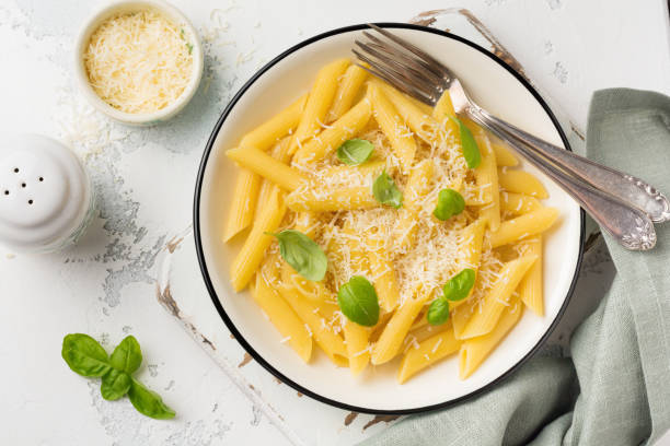 istock Penne rigate pasta with parmesan cheese and basil leaves in ceramic dish on light old concrete background. Selective focus. 984134442