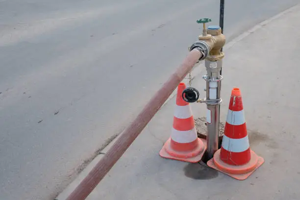 Water hydrant with hose and traffic cones at a sidewalk