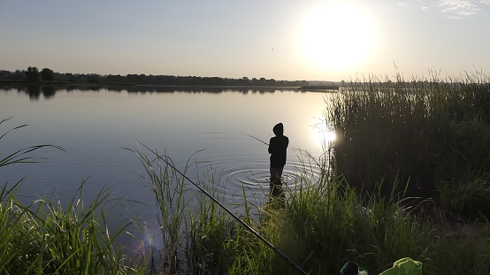 A man with a fishing rod on the shore of the lake is catching fish. Fishermen on the shore of the lake in the sun.